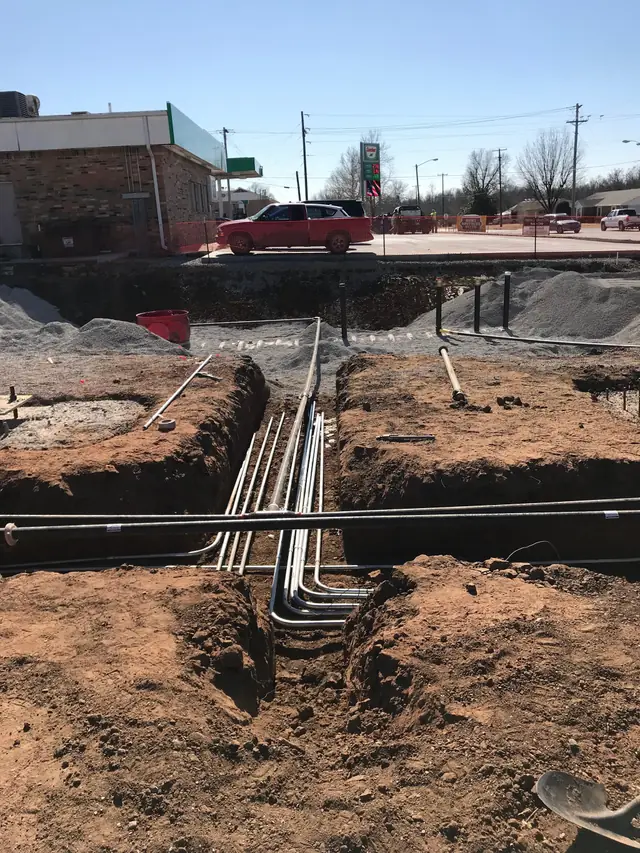 Conduit runs laid into an open trench at a commercial job site in Payne County
